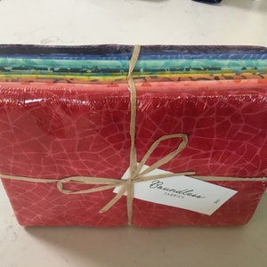 May include: A stack of colorful fabric bundles wrapped in clear plastic and tied with twine. The fabric has a variety of patterns and colors, including red, blue, and yellow. A tag that says "Boundless Fabrics" is attached.