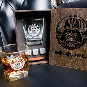 May include: A wooden gift box with a dark wood finish. The box contains two square glasses with a Darth Vader design and the name "Michael" engraved on them. The box also includes four ice cubes. The box has a Darth Vader design on the front with the name "Michael" engraved on it.