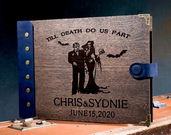May include: Wooden photo album with a dark finish, featuring a laser-etched design of a couple and bats, with the text "TILL DEATH DO US PART," names, and a date. The album has a blue leather spine and closure with brass accents.