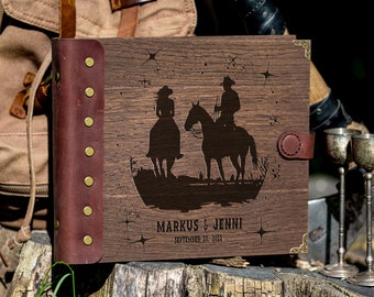 Peut inclure: Un album photo en bois avec une couverture en cuir marron et des accents en laiton. Le devant de l'album présente un motif gravé au laser d'un couple à cheval sous un ciel étoilé. Le texte "Markus & Jenni September 10, 2022" est gravé sous l'image.