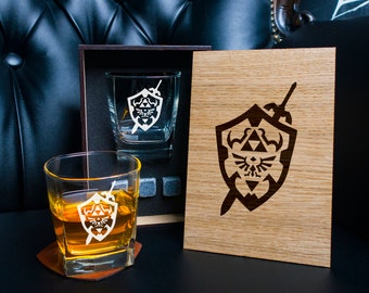 May include: A wooden box set with two etched glass whiskey tumblers featuring the Triforce symbol from the Legend of Zelda video game series. The box also has a wooden panel with the Triforce symbol etched into it.