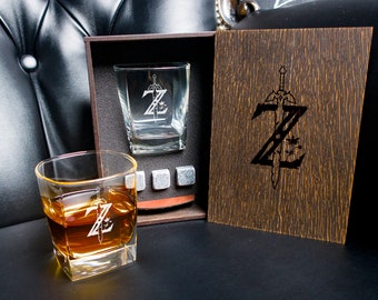 May include: A wooden box set with two engraved whiskey glasses, four whiskey stones, and a lid with a sword and letter Z design.