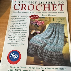 May include: A Boye instructional booklet titled I Taught Myself To Crochet, featuring a blue and white variegated afghan on the cover. The cover includes text about 19 patterns, 3 bonus projects, and a special left-handed section included.