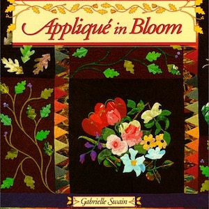 May include: A book titled "Appliqué in Bloom" by Gabrielle Swain. The cover features a colorful floral design with red, pink, yellow, and blue flowers on a black background. The book is part of a series called "That Patchwork Place".