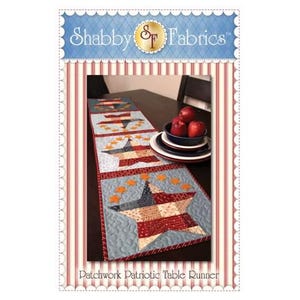 May include: A patchwork patriotic table runner with a star and stripe design. The runner features a blue background with orange stars and a large star in red, white, and blue. The text "Shabby Fabrics" is at the top.