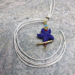 Medium-length handmade necklace with white lanyard and navy blue bead in a shape of starfish with bronze elements.