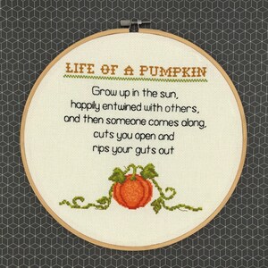 Könnte beinhalten: Ein weißer Stickrahmen mit einem Kreuzstich-Design, das einen Kürbis mit dem Text "LIFE OF A PUMPKIN" und einem Gedicht über den Lebenszyklus eines Kürbisses darstellt.