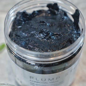 May include: A close-up of a black charcoal face mask in a clear jar with the label "PLUMP ST CHARCOAL MASK" visible.