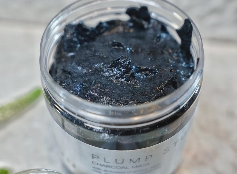 May include: A close-up of a black charcoal face mask in a clear jar with the label "PLUMP ST CHARCOAL MASK" visible.