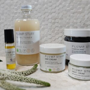 May include: A set of five skincare products in white jars and bottles with the brand name "Plump Stuff" printed on the labels. The products include a facial toner, eye serum, day cream, charcoal mask, and night cream.