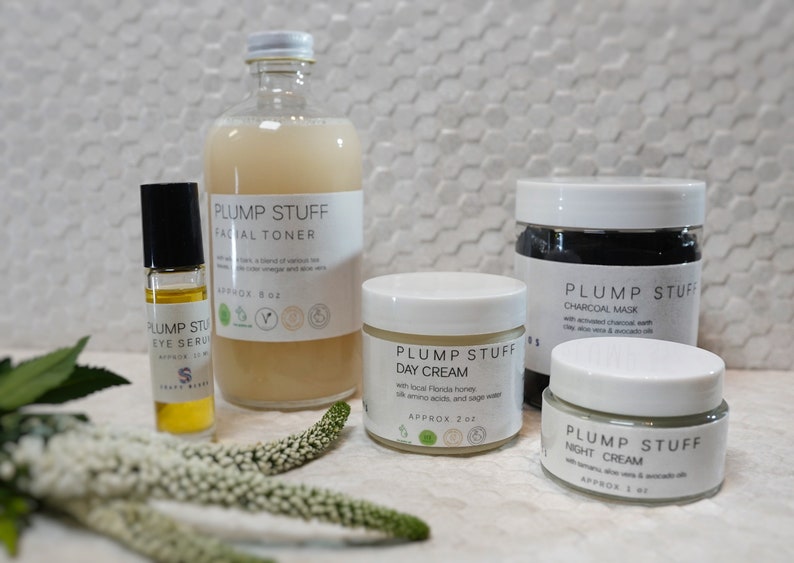 May include: A set of five skincare products in white jars and bottles with the brand name "Plump Stuff" printed on the labels. The products include a facial toner, eye serum, day cream, charcoal mask, and night cream.