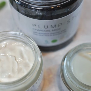 May include: Three glass jars with white cream inside. The jar in the center has a black label that reads "PLUMP ST CHARCOAL MASK".