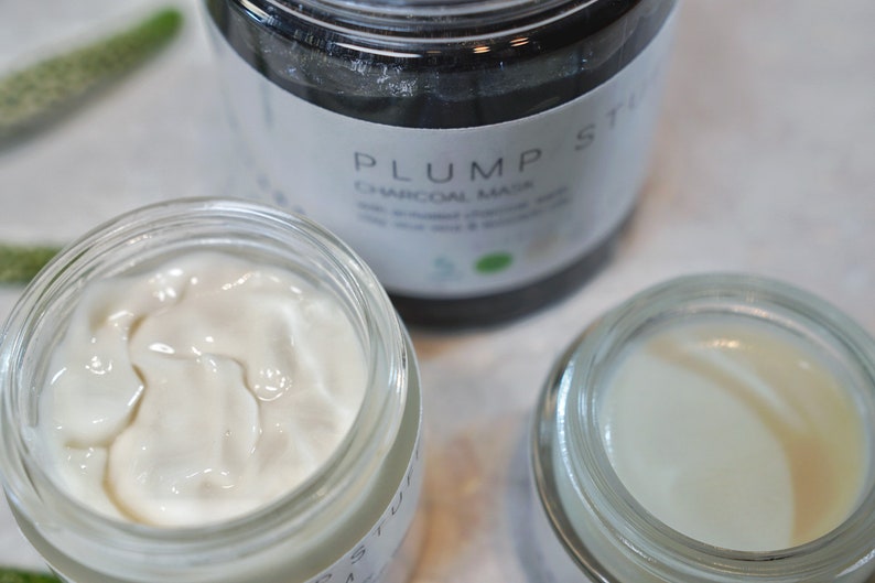 May include: Three glass jars with white cream inside. The jar in the center has a black label that reads "PLUMP ST CHARCOAL MASK".