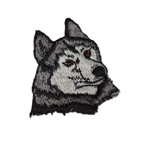 May include: Embroidered patch of a wolf's head with black and gray fur, brown eyes, and a white muzzle.