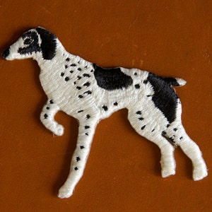 May include: White and black embroidered patch of a dog, possibly a pointer, with a white background and black spots.