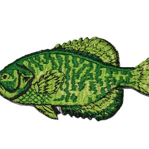 May include: Embroidered patch featuring a green fish with detailed scales and fins. The fish has a textured appearance with varying shades of green, and is set against a white background. The patch is likely designed for application on clothing or accessories.