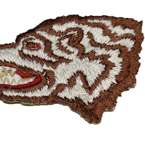 May include: Brown and white embroidered patch of a wolf's head with red teeth.