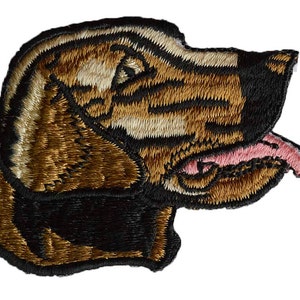 May include: Embroidered patch featuring a dog's head in profile. The patch showcases a brown and tan dog with black accents and a pink tongue. The design is detailed with textured stitching, creating a realistic depiction of the canine.