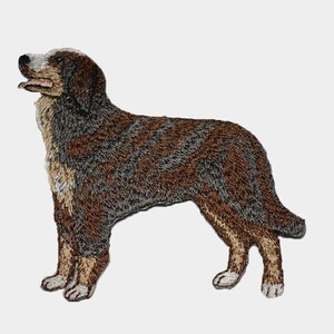 May include: Embroidered patch of a dog in a standing pose. The dog has a brown and gray patterned coat, with tan and white accents on the legs, chest, and face. The dog's mouth is slightly open, and its tongue is visible.