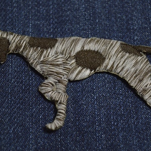 May include: A brown and white embroidered patch of a German Shorthaired Pointer dog running. The patch is on a blue denim background.