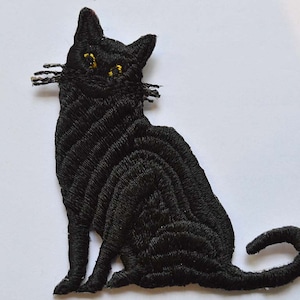 May include: Black embroidered iron-on patch of a sitting cat with yellow eyes.