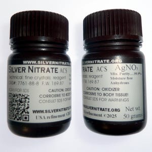 May include: Two dark brown bottles of Silver Nitrate ACS reagent. Each bottle has a black cap and a white label with text including the chemical formula AgNO3, and the website address www.SILVERNITRATE.org. One bottle contains 50 grams.