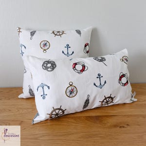 May include: Two white rectangular throw pillows with a nautical theme. The pillows are decorated with watercolor illustrations of anchors, compasses, ship wheels, life preservers, and rope knots in shades of blue, red, and brown.