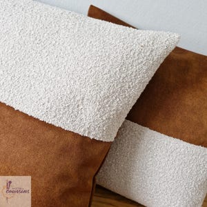 Peut inclure: Deux coussins décoratifs avec un tissu en daim brun et un tissu texturé blanc. Les coussins sont disposés sur une surface brun clair.