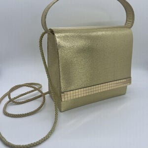 May include: A gold-colored handbag with a chain strap and a gold-toned clasp. The bag has a textured surface and a rectangular shape.