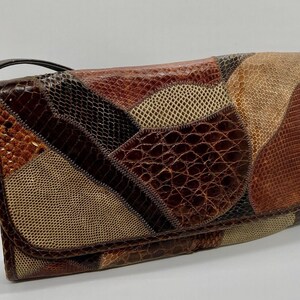 May include: A brown leather patchwork clutch purse with a strap. The purse is made of different types of snakeskin.