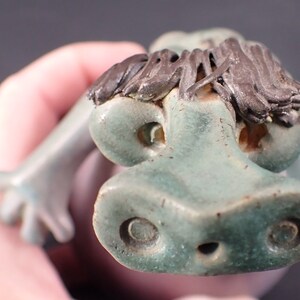 Abstract Clay and Ceramic Green Tone Dinosaur Long Stringy Hair Emerging from his Shell Purple Tone