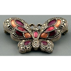 May include: A silver-toned butterfly brooch with marcasite accents. The wings feature a combination of red, orange, and purple enamel. The brooch is a decorative accessory.