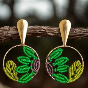 May include: A pair of gold dangle earrings with green and purple macrame flower designs in a circular frame.