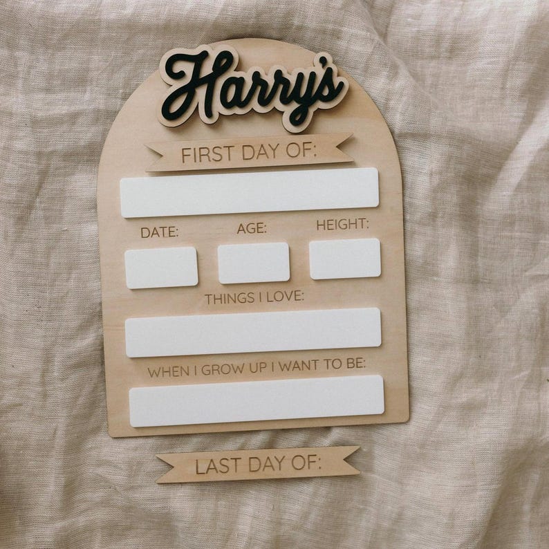 Op de afbeelding: Een houten bord met de naam "Harry's" in zwarte letters. Het bord heeft ruimte om informatie in te vullen over de eerste en laatste dag van iets, zoals een schooljaar of het eerste jaar van een baby. Het bord bevat de tekst "Eerste Dag Van:", "Datum:", "Leeftijd:", "Lengte:", "Dingen Die Ik Leuk Vind:", "Wanneer Ik Groot Ben Wil Ik Zijn:", en "Laatste Dag Van:".