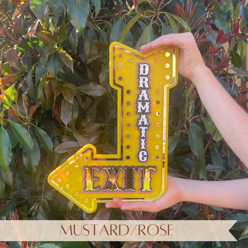 Features mustard acrylic "Dramatic Exit" arrow sign with gold mirror accents. Motivational, empowering decor for eclectic, industrial, modern, bright, and boho spaces. Perfect for bedrooms, salons, craft rooms, cafes, and gift for confident women. Customizable arrow direction & color. Bright, bold, confidence-boosting home decor, dopamine decor art, quirky wall hanging, vintage marquee wall art, inspiring wall decor, affirmation sign, motivational decor, eclectic home decoration.