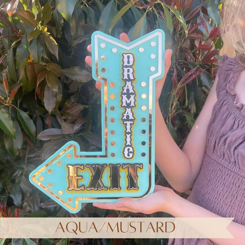 Features aqua acrylic "Dramatic Exit" arrow sign with gold mirror accents. Motivational, empowering decor for eclectic, industrial, modern, bright, and boho spaces. Perfect for bedrooms, salons, craft rooms, cafes, and gift for confident women. Customizable arrow direction & color. Bright, bold, confidence-boosting home decor, dopamine decor art, quirky wall hanging, vintage marquee wall art, inspiring wall decor, affirmation sign, motivational decor, eclectic home decoration.
