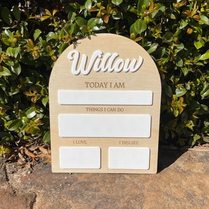 以下が含まれることがあります： 白い筆記体で「Willow」と書かれた木製のアーチ型の看板。看板には、「今日は」「できること」「好き」「嫌い」と書くための空白スペースがあります。