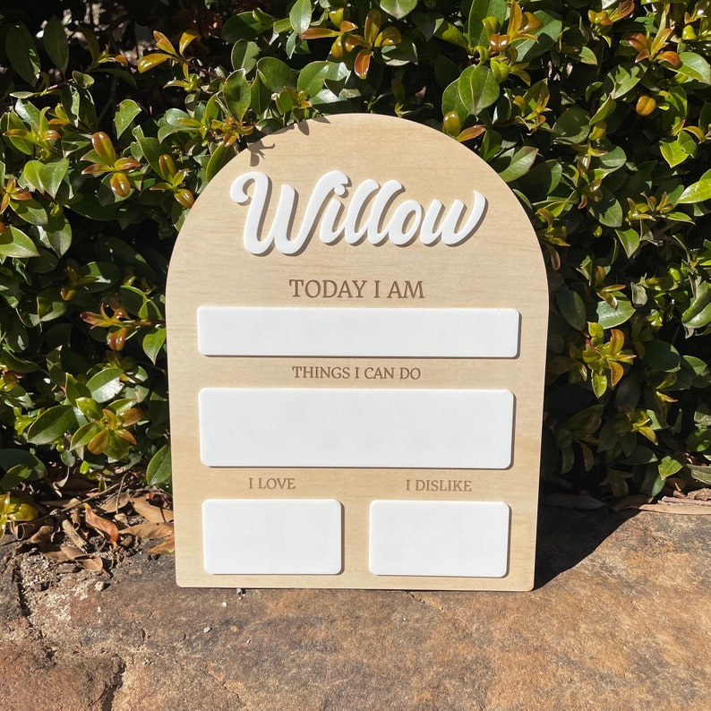 以下が含まれることがあります： 白い筆記体で「Willow」と書かれた木製のアーチ型の看板。看板には、「今日は」「できること」「好き」「嫌い」と書くための空白スペースがあります。
