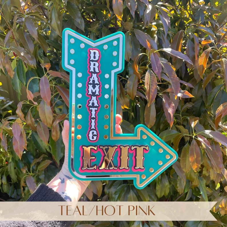 Features teal and hot pink acrylic "Dramatic Exit" arrow sign with gold mirror accents. Motivational, empowering decor for eclectic, industrial, modern, bright, and boho spaces. Perfect for bedrooms, salons, craft rooms, cafes, and gift for confident women. Customizable arrow direction & color. Bright, bold, confidence-boosting home decor, dopamine decor art, quirky wall hanging, vintage marquee wall art, inspiring wall decor, affirmation sign, motivational decor, eclectic home decoration.