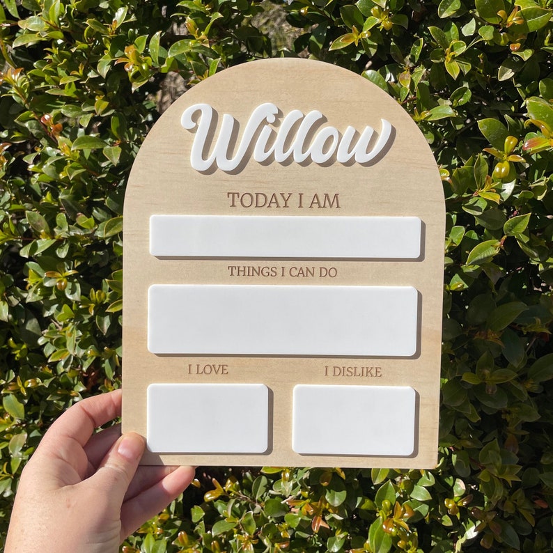 以下が含まれることがあります： 白い筆記体で「Willow」と書かれた木製のアーチ型の看板。看板には、「今日は」「できること」「好き」「嫌い」と書くための空白スペースがあります。