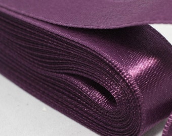 May include: A roll of deep purple satin ribbon. The ribbon is folded and stacked, showing the smooth, shiny surface.