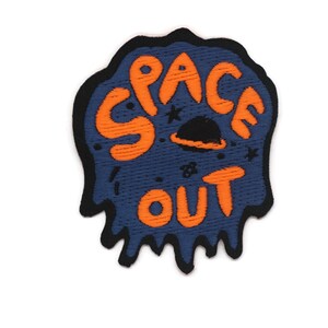 May include: A blue and orange embroidered patch with the text "SPACE OUT" in a dripping font. The patch features a small black and orange spaceship with stars.