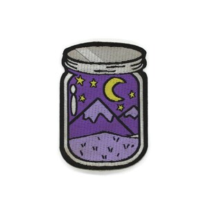 May include: A purple glass jar with a silver lid containing a night sky scene with a crescent moon, stars, and purple mountains.