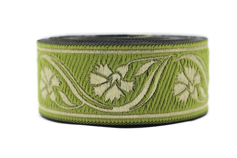 May include: A roll of decorative ribbon featuring a floral design. The ribbon has a light green background with a cream-colored floral pattern. The edges are black. This ribbon is suitable for crafts and embellishments.