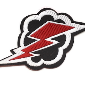 May include: A black and white embroidered patch featuring a red lightning bolt within a white cloud. The patch is iron-on and can be used to customise clothing, bags, or other items.