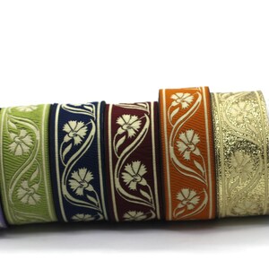 May include: A collection of decorative ribbons in various colors, including lavender, green, navy, burgundy, orange, gold, and silver. Each ribbon features a floral design with a repeating pattern. The ribbons are rolled up, showcasing their intricate details.