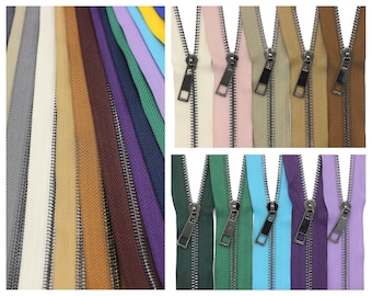 Könnte beinhalten: Sortiment von Reißverschlussbändern in verschiedenen Farben, darunter Grau, Beige, Braun, Rotbraun, Lila, Blau, Grün und Rosa. Die Reißverschlüsse haben silberne Metallzähne und Schieber.