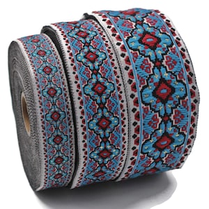 Op de afbeelding: Een rol decoratief lint met een herhalend patroon. Het lint heeft een ontwerp met rode, blauwe en gouden accenten op een witte achtergrond. Het lint is waarschijnlijk bedoeld voor knutselen, naaien of cadeauverpakking.