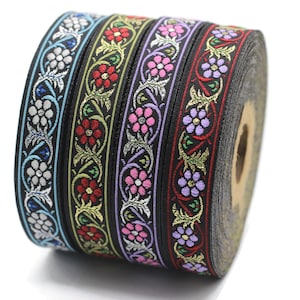 Puede incluir: Un rollo de cinta decorativa con fondo negro y patrones florales en varios colores. La cinta presenta flores en blanco, rojo, rosa y morado, con detalles dorados y verdes. La cinta se utiliza probablemente para manualidades o adornos.