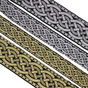 Pode incluir: Close-up de fita decorativa em ouro e prata. A fita apresenta um design de nó celta com fundo preto. A fita dourada está na parte inferior e a prateada na superior. As fitas têm aproximadamente 2,5 cm de largura.